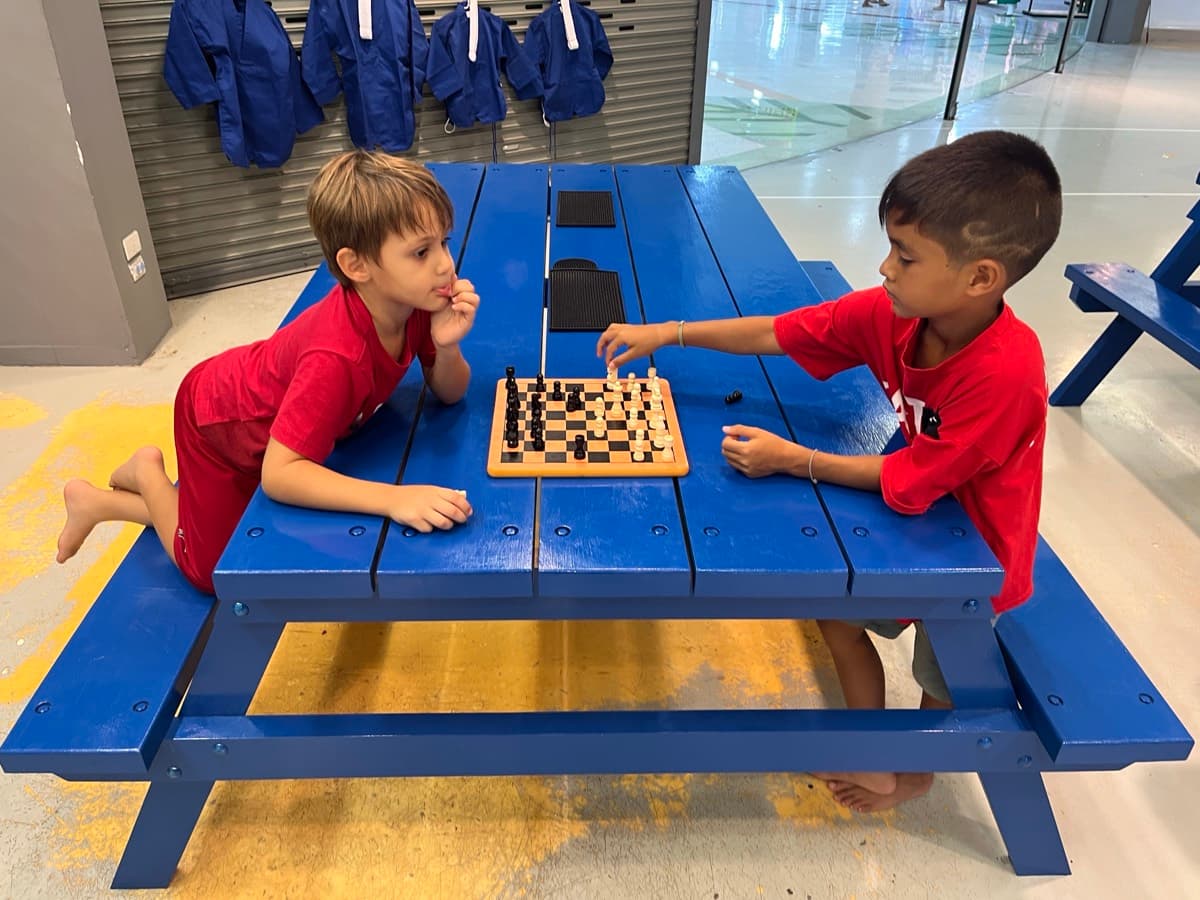 Two kids playing chess at the blue table